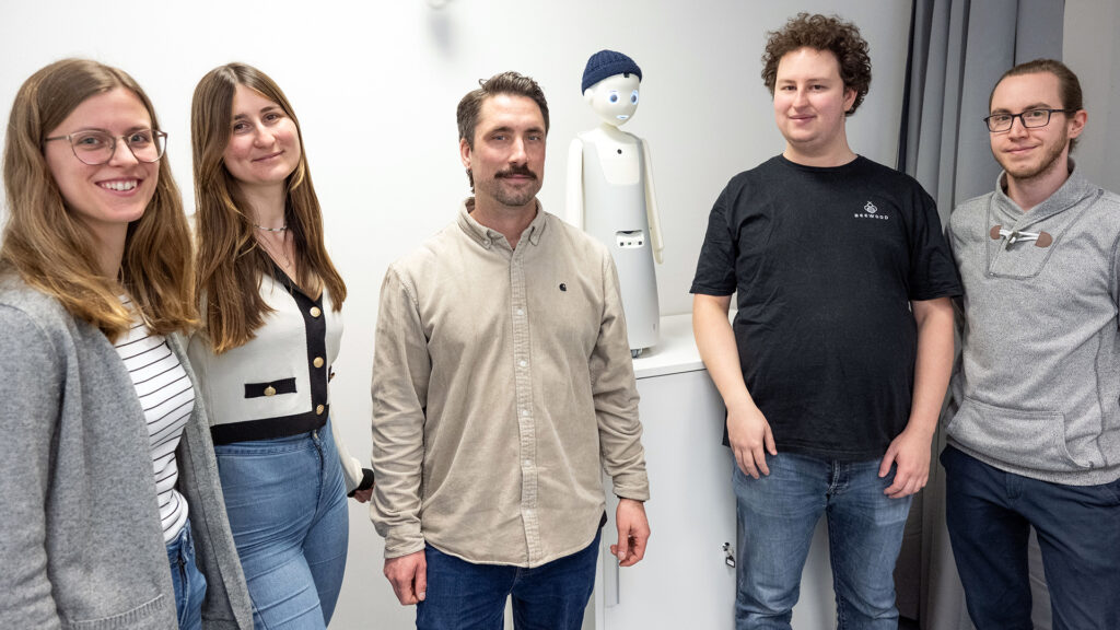 Bild in Originalgröße ansehen (v.l.) Masterstudentin Katharina Stiller, Doktorandin Hannah Großwieser (mittlerweile Uni Linz), Prof. Dr. Johannes Kraus, Roboter Navel, Michel Schiszler und Tim Niewalda (Foto: Peter Thomas)