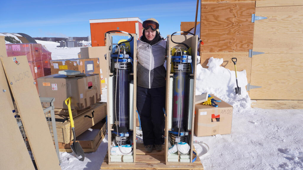 Lea Schlickmann mit zwei der von ihr entwickelten und getesteten WOMs-Module, die ins antarktische Eis eingebracht werden (Foto/©: Andreas Nöll / IceCube/NSF)